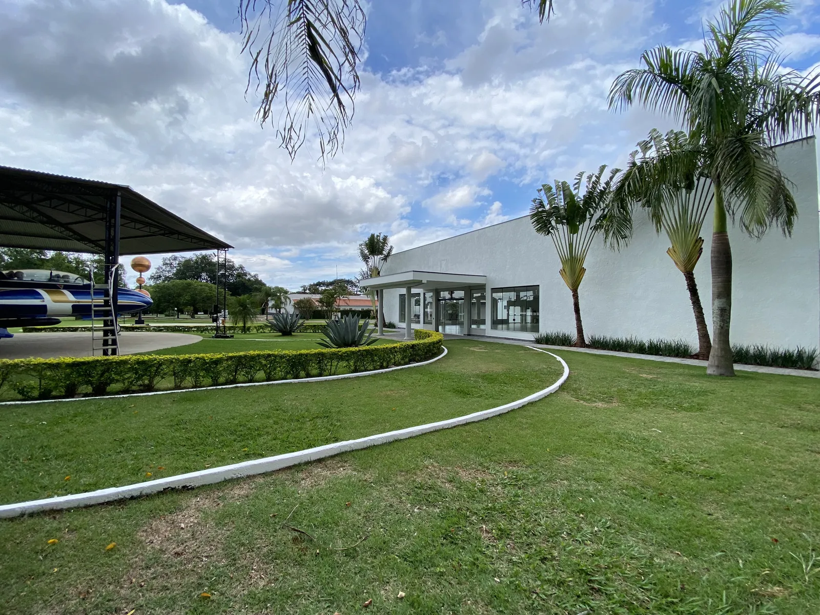Jato T-33 exposto sob cobertura própria ao lado do salão branco, entre jardins
