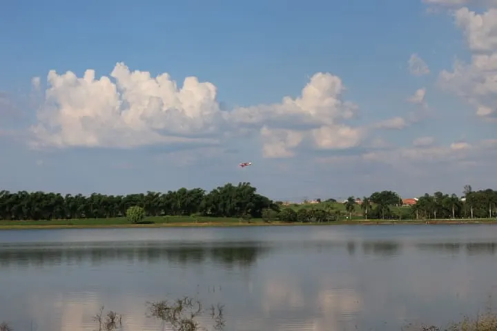 Vista aberta do lago com mata ao fundo e avião pequeno cruzando o céu