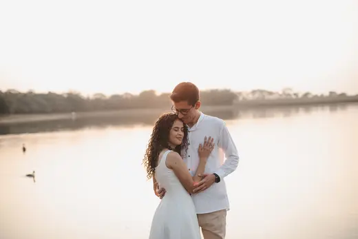 Casal abraçado à beira do lago espelhado ao entardecer